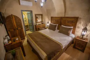 Taş kemerli otel odası, el oyması ahşap yatak başlığı, otantik komodin ve rustik aydınlatmalı butik cave hotel interior dekorasyon tasarımı