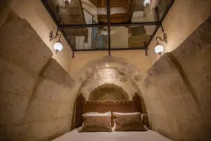 Taş kemerli otel odası dekorasyonu, oymalı ahşap yatak başlığı, tarihi taş duvar mimarisi ve butik cave hotel konseptli etnik interior tasarım mobilyaları