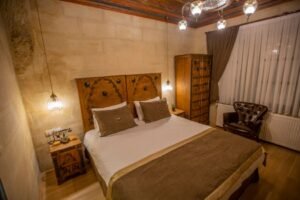 Masif ahşap yatak başlığı, taş duvarlı butik otel odası, rustik avize aydınlatması, oymalı gardırop ve etnik interior dekorasyon mobilya tasarımı